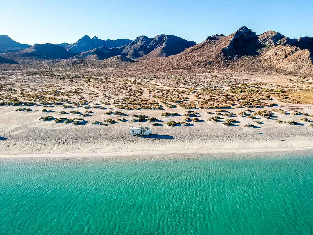 RV parked on a white sandy beach with mountains in the background